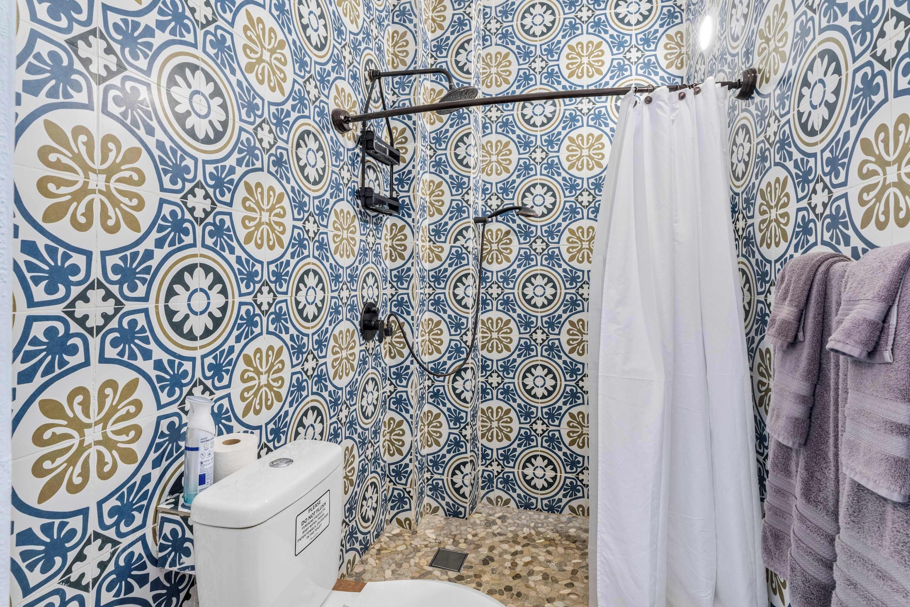 A bathroom with patterned tiles, a shower, a toilet, and a towel rack.
