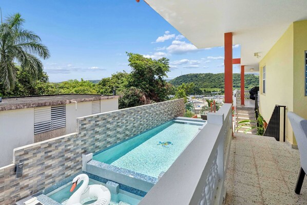 Una piscina sul tetto con un galleggiante a forma di cigno, un muro piastrellato e vista sul verde circostante.