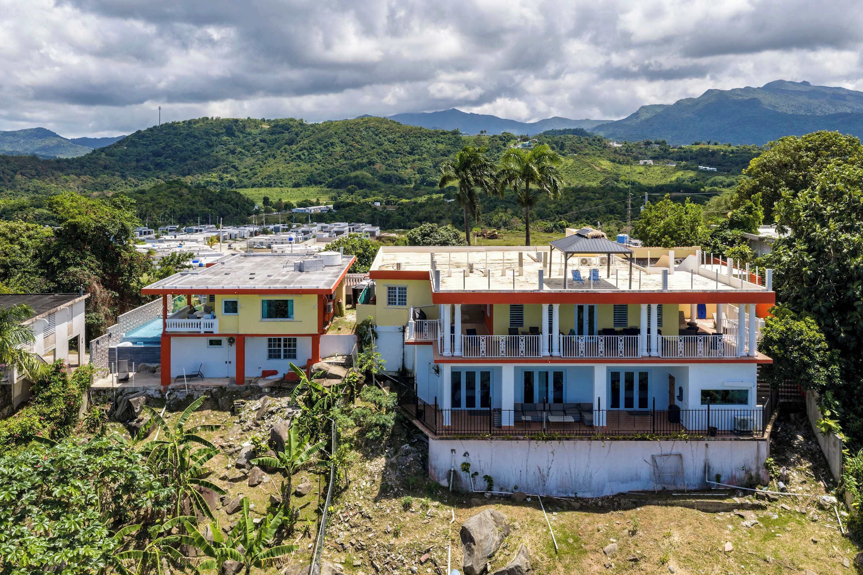 Um edifício residencial com varanda, rodeado por vegetação e montanhas.