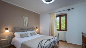 Ein Schlafzimmer mit einem Bett, Nachttischlampen, einer Wanddekoration aus Wandteppich, einem Fenster mit Vorhängen und einer Heizung.