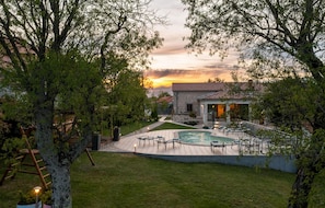 A pool area with a stone building in the background, surrounded by trees and a sunset. - Beautiful home in Nedescina with WiFi (Nedescina)