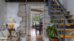 Ein gemütliches Wohnzimmer mit einem Steingewölbe, einer Holztreppe und einem Essbereich im Hintergrund.