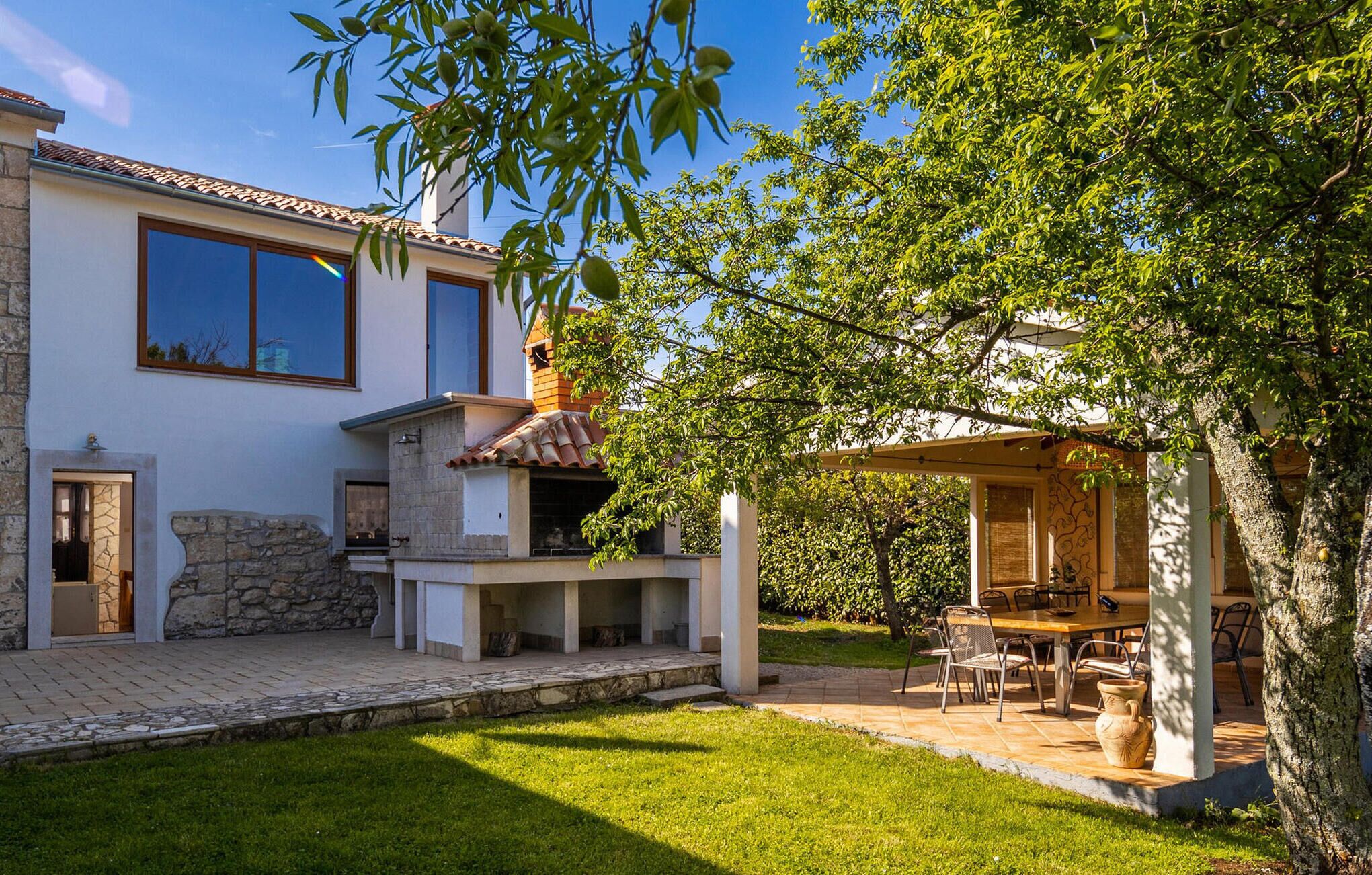 A house with a stone exterior, a patio with a table and chairs, and a covered outdoor area.