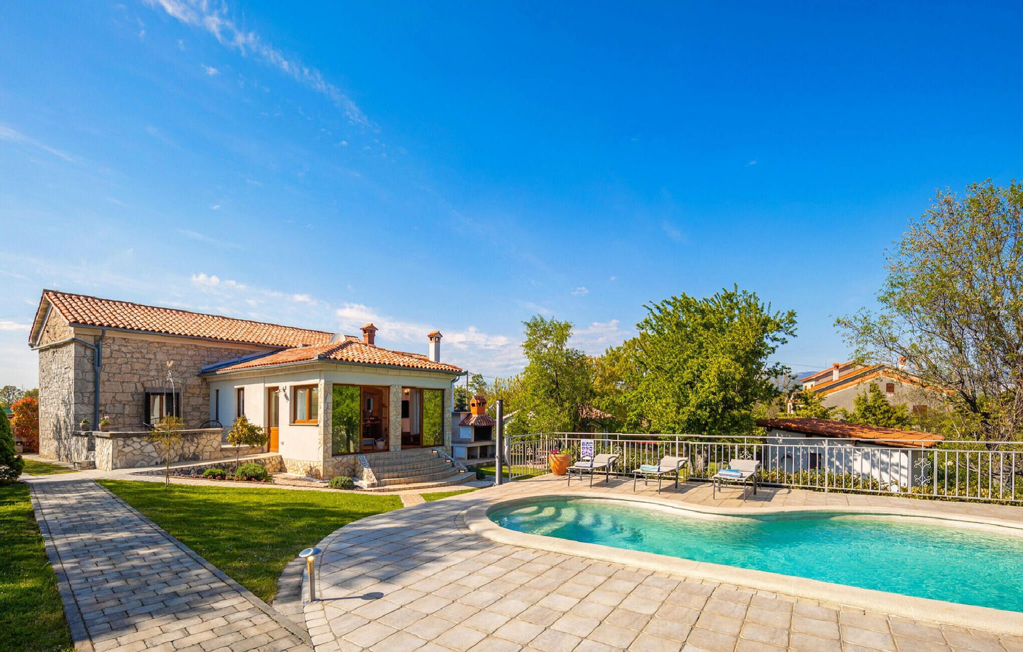 Une maison avec une façade en pierre, un toit en tuiles et une piscine équipée de chaises longues.