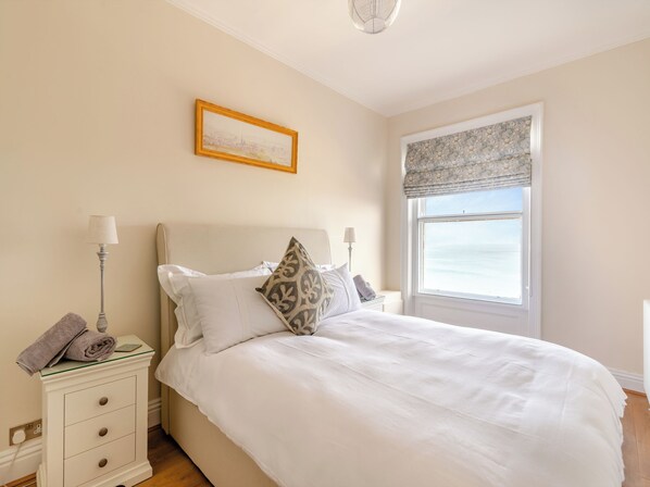 A bedroom with a bed, a nightstand, a lamp, a window with a view, and a framed picture on the wall.