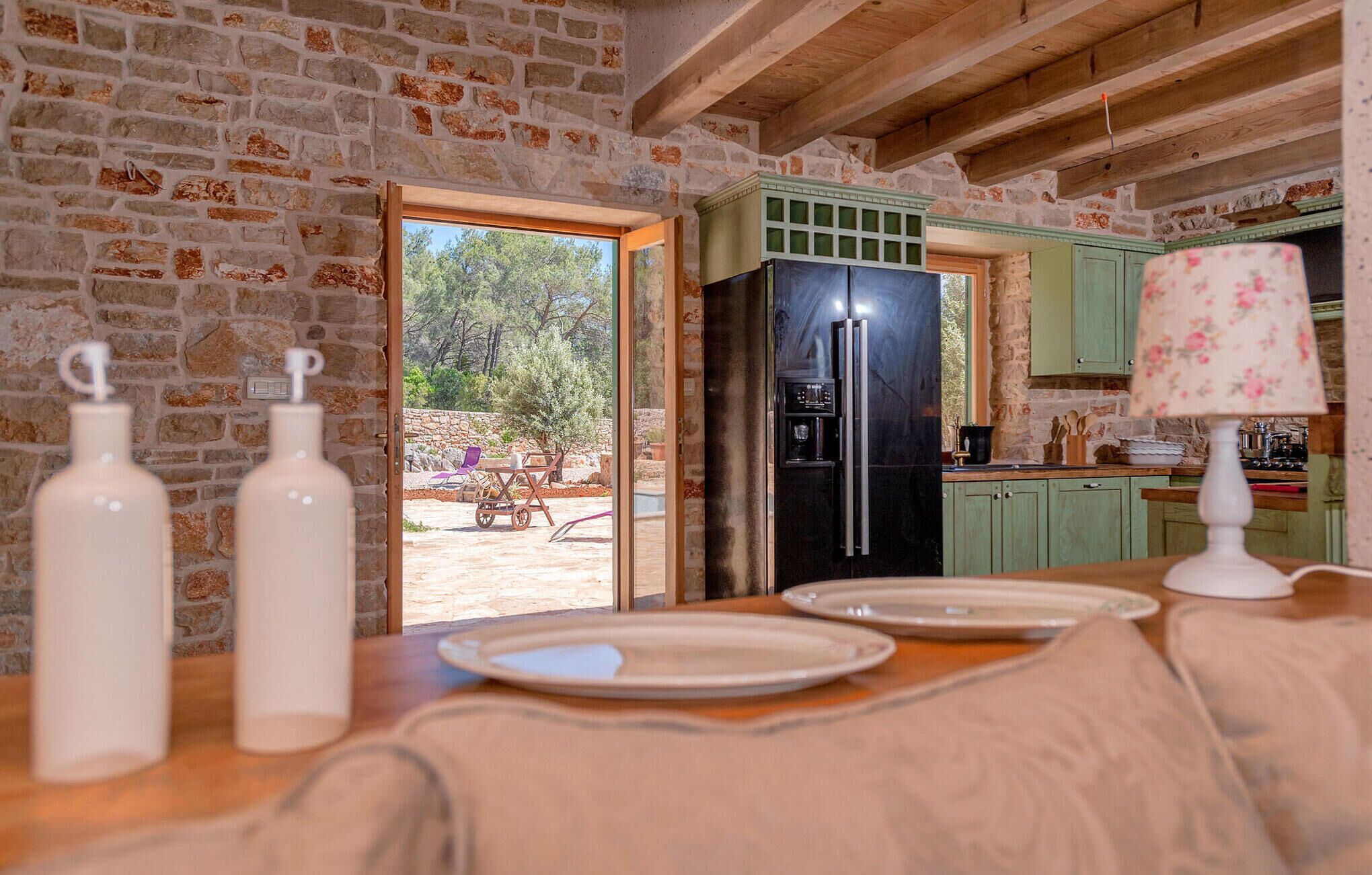 Une cuisine rustique avec un mur en pierre, un réfrigérateur noir et un coin repas avec une table dressée pour deux personnes.