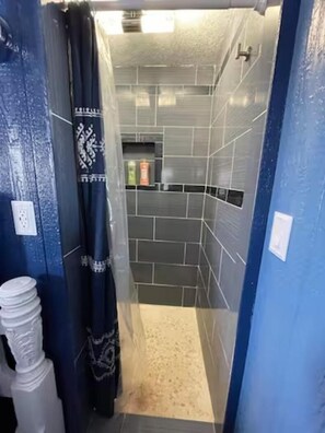 Un baño estrecho con paredes azules, zona de ducha con paredes de azulejos y un inodoro a la izquierda.
