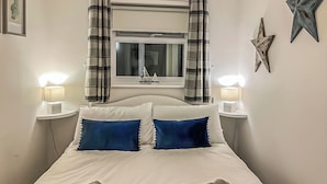 Un lit bien fait, avec deux oreillers, deux lampes de chevet, une fenêtre avec des rideaux et une décoration en forme d’étoile sur le mur.