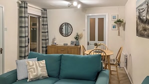 Un salon avec un canapé de couleur turquoise, une table à manger en bois et des chaises. Un miroir est accroché au mur, et une porte est dotée de panneaux en verre dépoli.