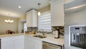 A modern kitchen with white cabinetry, a stainless steel dishwasher, a built-in water dispenser, and a stone backsplash. - Spacious Baton Rouge Home Rental: 12 Mi to LSU! (Baton Rouge)
