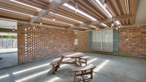 A covered patio area with a wooden table and benches, brick walls, and a window with shutters. - Spacious Baton Rouge Home Rental: 12 Mi to LSU! (Baton Rouge)