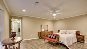 A bedroom with a bed, a nightstand, a dresser, a red sofa, and a wooden table. - Spacious Baton Rouge Home Rental: 12 Mi to LSU! (Baton Rouge)