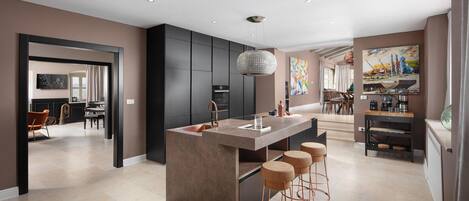 A modern kitchen with a central island, bar stools, and a dining area with a view.