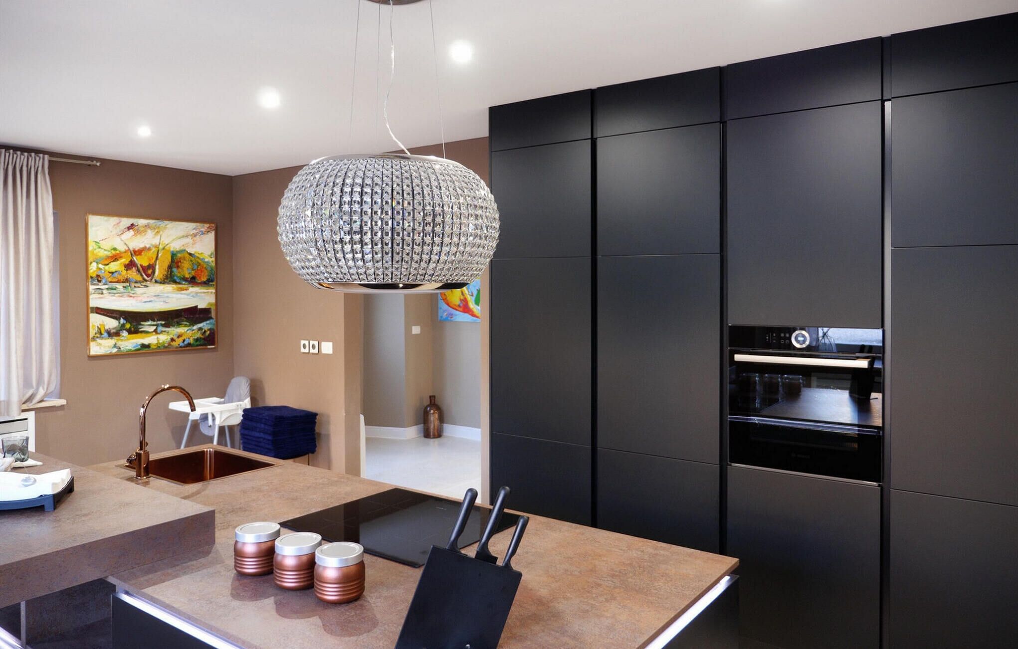 A modern kitchen with a black oven, a stainless steel sink, and a large chandelier.