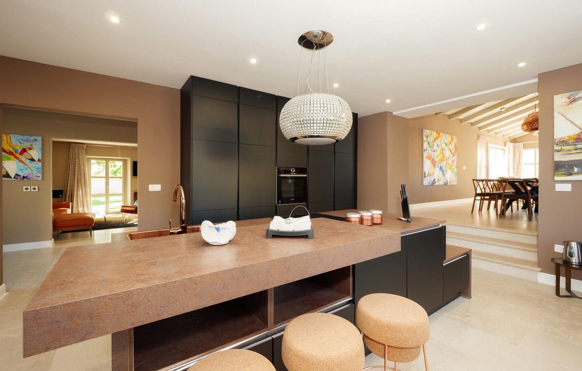 Una cocina moderna con una isla central, muebles oscuros y una lámpara de araña.