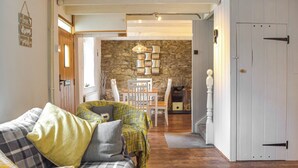 A cozy living room with a sofa, a dining table, and a stone wall. - 2 bedroom accommodation in Cwrt-newydd (Cwrt-newydd)