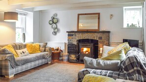 A cozy living room with a stone fireplace, two sofas with plaid upholstery, and a large window providing natural light. - 2 bedroom accommodation in Cwrt-newydd (Cwrt-newydd)