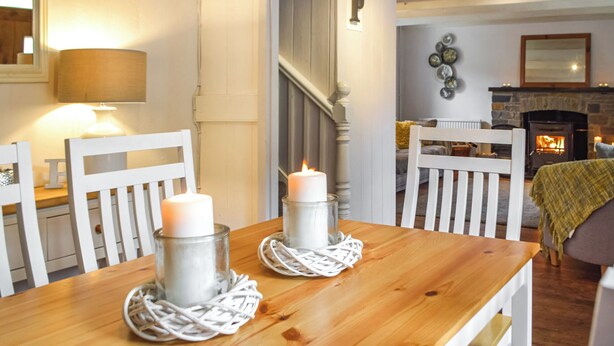 A dining area with a wooden table, white chairs, and candles. A staircase is visible in the background. - 2 bedroom accommodation in Cwrt-newydd (Cwrt-newydd)