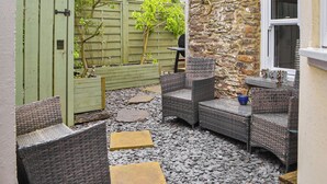 A patio area with wicker furniture, a stone wall, and a green gate. - 2 bedroom accommodation in Cwrt-newydd (Cwrt-newydd)