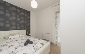 Une chambre à coucher comprenant un lit, une table de chevet, une lampe, un radiateur et une fenêtre avec des rideaux.