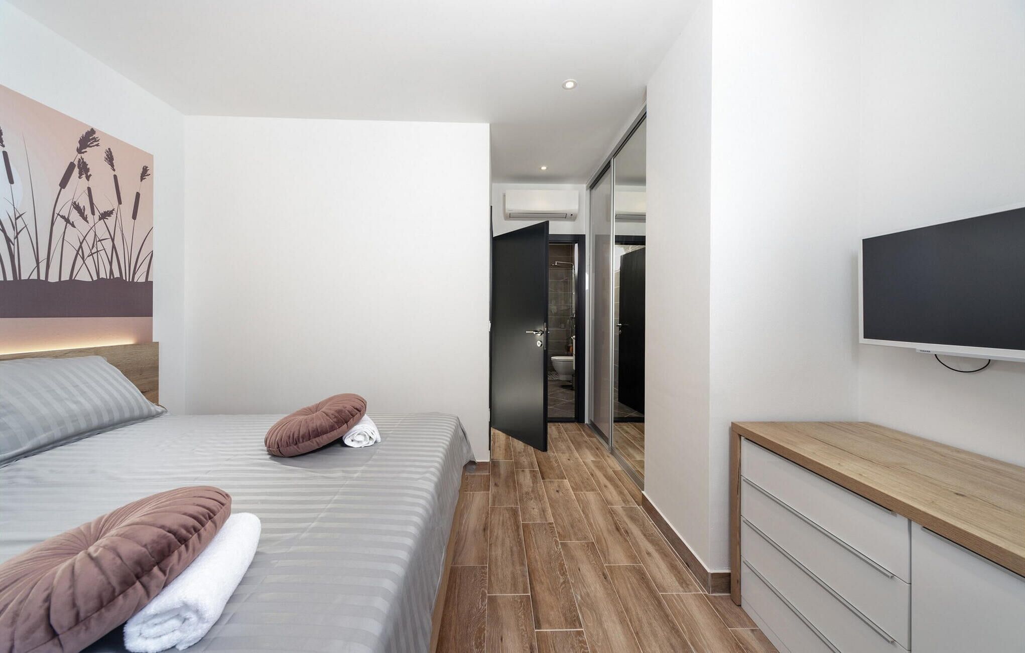 Ein modernes Hotelzimmer mit Bett, Flachbildfernseher, Holzkommode und einem Gemälde an der Wand.