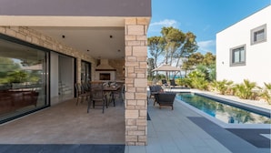 Eine moderne Außenpatio mit Pool, Steinpfeilern und einem Essbereich mit Stühlen und einem Tisch.
