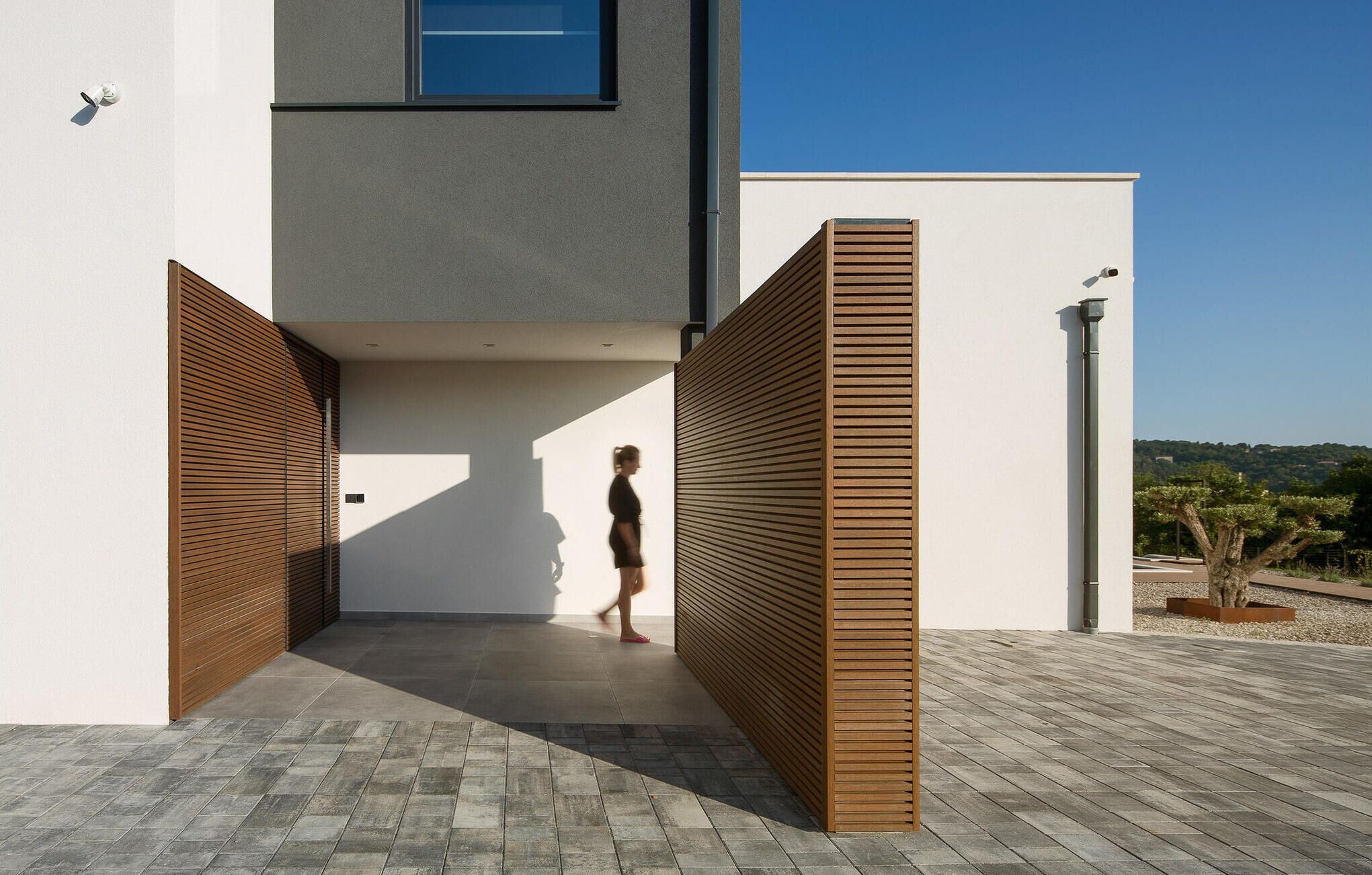 Un bâtiment moderne avec une entrée étroite, un portail en bois à lattes et un ciel dégagé.
