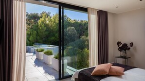 Un dormitorio moderno con un amplio ventanal corredera que da a un balcón con piscina y vegetación.