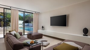 Una sala de estar moderna con un televisor grande, asientos cómodos y vista a una piscina al aire libre.