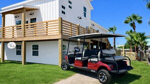 A two-story building with a white exterior and a wooden deck. A red golf cart is parked in front.