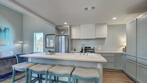 A modern kitchen with a central island, bar stools, a refrigerator, and a stove.