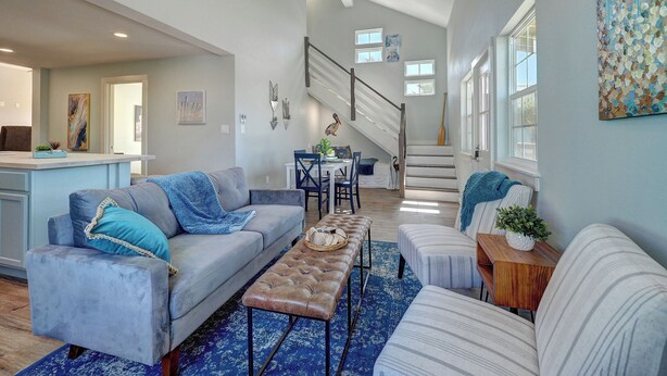 A spacious living area with a gray sofa, a coffee table, and a striped ottoman. A staircase leads to an upper level.