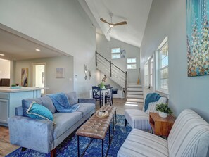 A spacious living area with a gray sofa, a coffee table, and a striped ottoman. A staircase leads to an upper level. - Pelican Beach House with 6-seater Golf Cart and private POOL! (Port Aransas)
