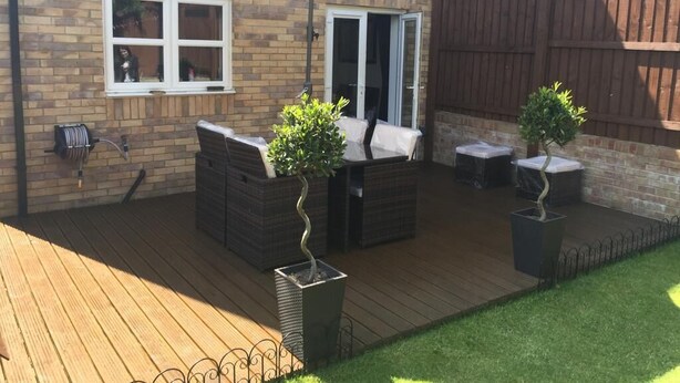 Um deck de madeira com móveis para área externa, um guarda-sol branco e plantas em vasos.