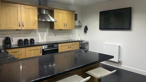 Uma cozinha moderna com armários de madeira, bancada preta, forno, máquina de café e uma TV preta fixada na parede.