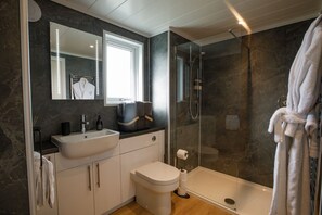 Features a sleek bathroom with a large mirror, white sink, toilet, and glass-enclosed shower.