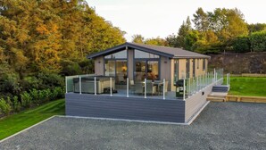 Eine moderne Terrassenanlage im Freien mit Grill, Sitzgelegenheiten und Blick auf den umliegenden Garten.