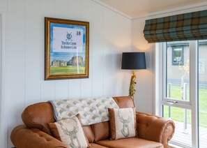 Relax in a stylish living room with a leather sofa, framed golf course view, and large window overlooking a green lawn.