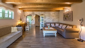 A cozy living room with a stone wall, wooden ceiling beams, a sofa, a coffee table, and a lamp. - Beautiful home in Tar (Tar)