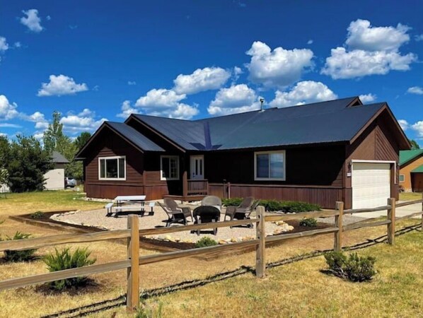 Situated in a serene grassy area, this cabin features a cozy front porch with a bench and table.