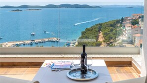 Een balkon met een tafel, een fles en twee glaasjes, met uitzicht op een jachthaven met boten en verre eilanden.