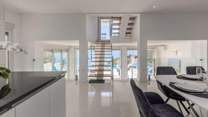 Een moderne keuken met een centraal eiland, een eethoek met een tafel en stoelen, en een trap naar een hoger gelegen verdieping.