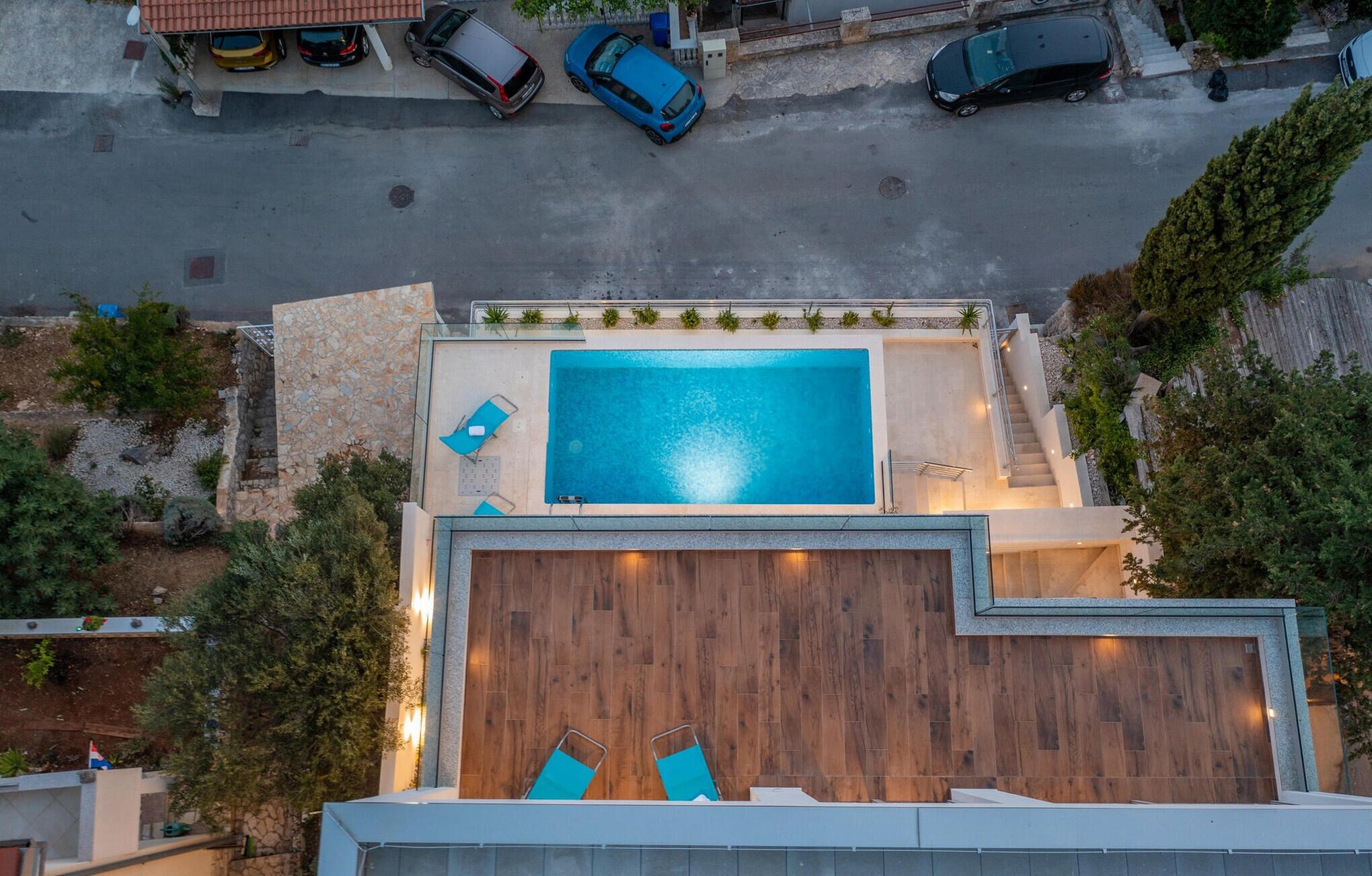 An aerial view of a modern residential property with a swimming pool, wooden deck, and a small staircase leading to a rooftop area.