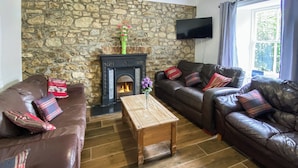 A living room with a stone wall, a fireplace, leather sofas, and a wooden coffee table.