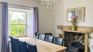 A dining area with a wooden table and black chairs, a stone fireplace, and a chandelier.