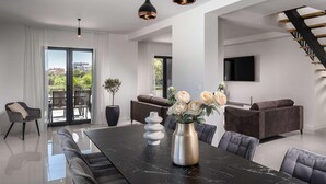 A modern living room with a large dining table, dark sofas, and a staircase. - 4 bedroom awesome home in Sukosan (Sukosan)