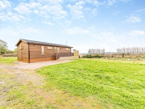 Une grange en bois, avec une allée de gravier et un champ verdoyant au premier plan.