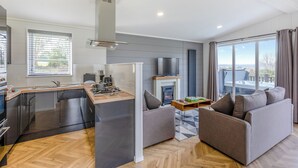 A modern kitchen with a central island, a dining area with a sofa, and a view of the outdoors through large windows. - 2 bedroom accommodation in Chadwick, near Worcester (Chadwick, near Worcester)