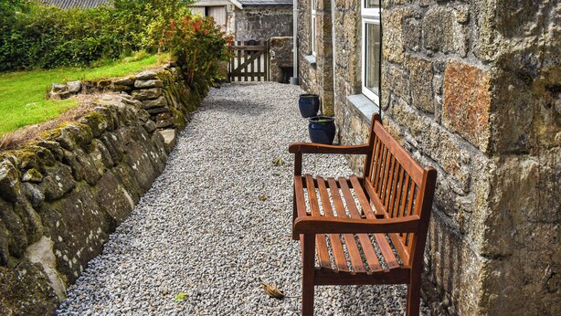 A stone building with a gravel path, a wooden bench, and a gate leading to a house. - 2 bedroom accommodation in Troon, near Camborne (Troon, near Camborne)