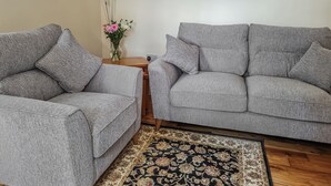 Two grey sofas, a wooden side table with a vase of flowers, and a patterned rug. - 2 bedroom accommodation in Troon, near Camborne (Troon, near Camborne)